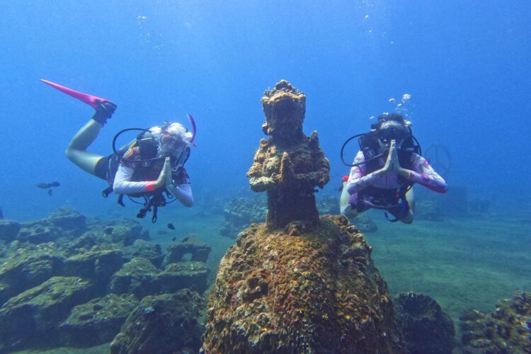 Two divers on each side of an underwater buddha figure