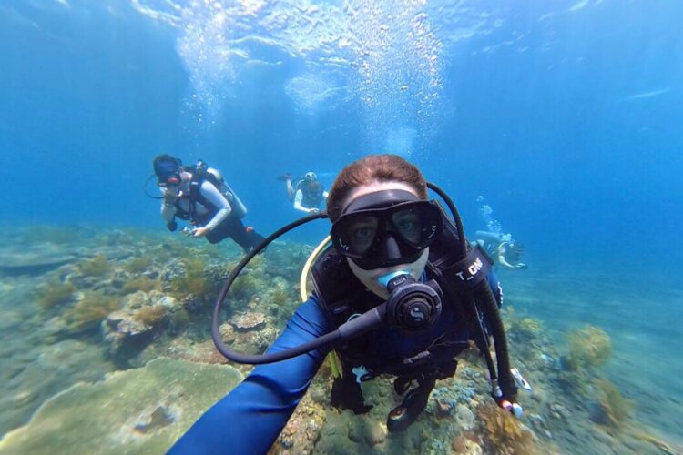 Volunteer diving above coral reef with other volunteers behind them