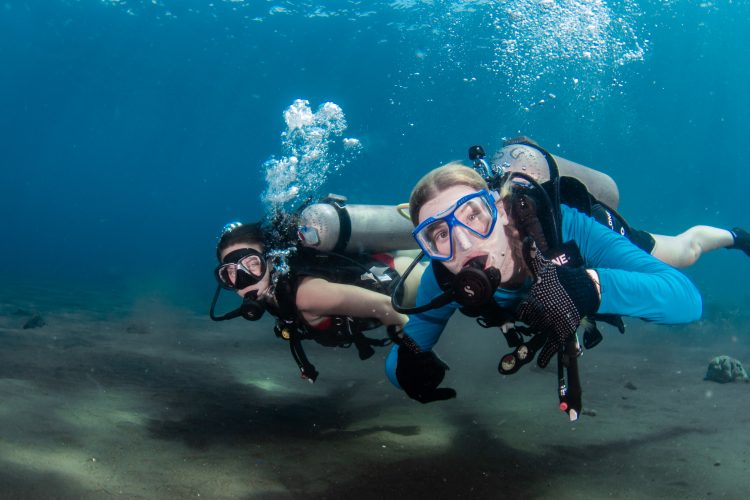 Two women divers underwater looking at photographer