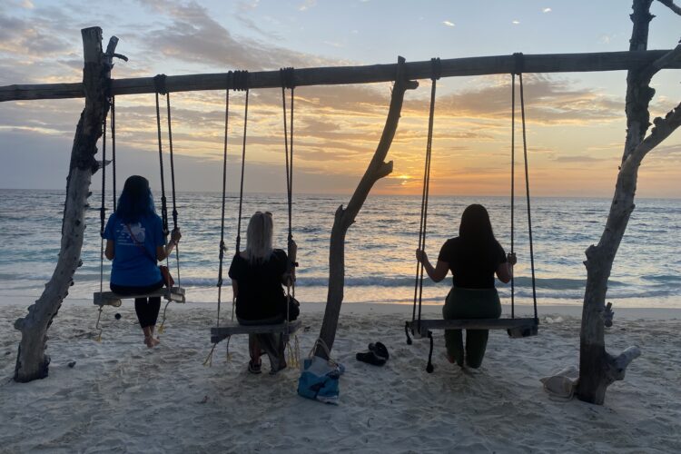 Volunteers sitting on swing on beach looking at the sunset over the sea