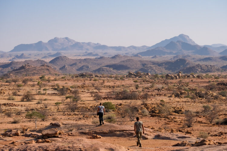 Two volunteers walking away in the desert landscape with mountains in the distance
