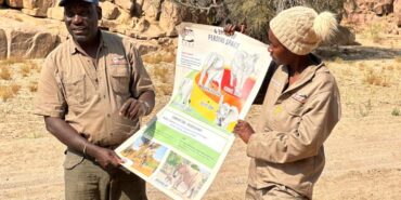 Two people holding up a large poster about elephant behaviour