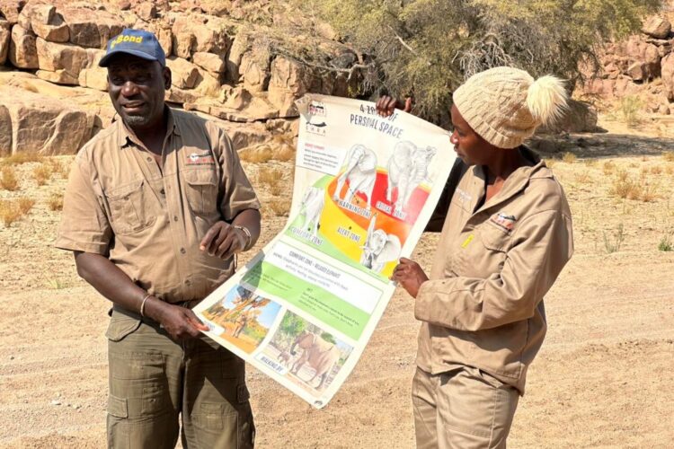 Two people holding up a large poster about elephant behaviour