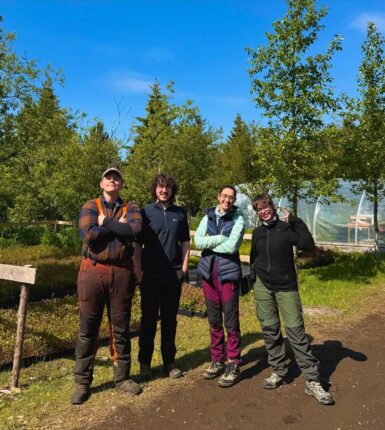Four voluneers standing next to each other with tall trees behind them