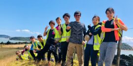 Group of volunteers standing next to each other along a fence with sea view in distance