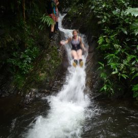 Volunteer sliding down waterfall in Ecuador