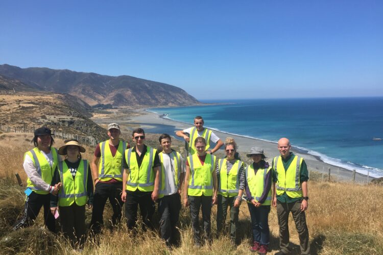 Group of volunteers in hi-vis vest standing next to each other with sea view in background