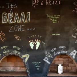 Blackboard with chalk writings on it above two stone pizza ovens