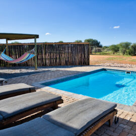 Wooden lounge chairs with pillows standing by the swimming pool area and hammocks in the background