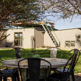 Round table with six chairs standing around it with white lodge building in the background