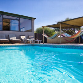 Water in blue swimming pool with lounge chairs and hammocks hanging in the background
